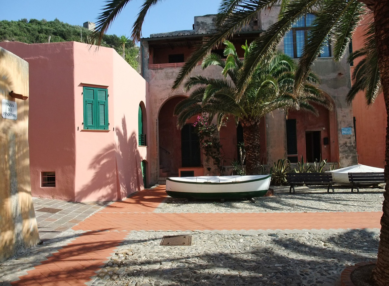 Una piazza lastricata di Varigotti, con un'imbarcazione da pesca, palme e case colorate in uno stile mediterraneo.